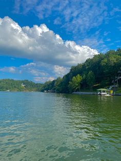 there is a boat that is in the water near some trees and clouds above it