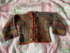 a knitted sweater laying on top of a pink bed spread with flowers and leaves