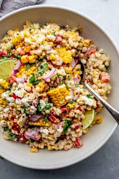 a white bowl filled with mexican corn salad and topped with cilantro, lime wedges