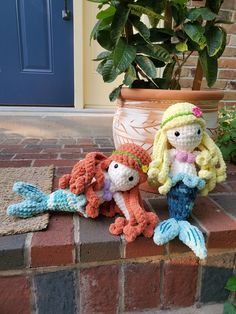 three crocheted mermaid dolls sitting next to a potted plant in front of a door