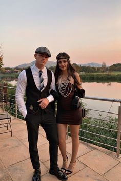 a man and woman standing next to each other on a bridge near the water at sunset