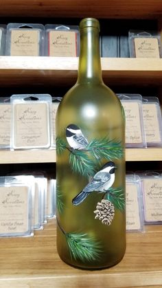 a glass bottle with birds painted on it sitting in front of some pine cones and other items