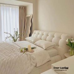 a white bed sitting in a bedroom next to a window filled with curtains and flowers