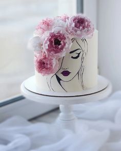 a white cake with pink flowers on top and a woman's face painted on it