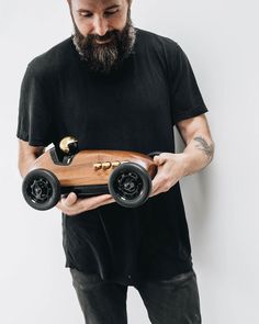 a bearded man holding a wooden toy car