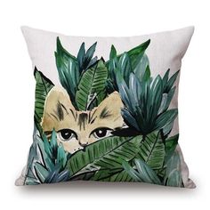 a pillow with an image of a cat peeking out from behind some green leaves on it