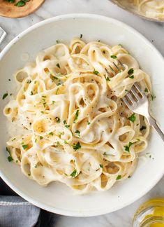 a white bowl filled with pasta and parsley on top of a marble countertop