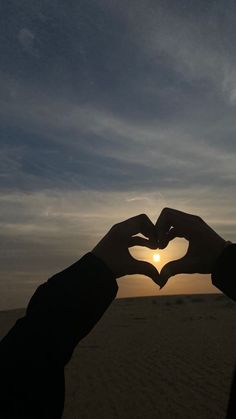 two hands making a heart shape with the sun setting in the back ground behind them