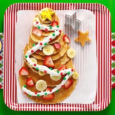 a christmas tree made out of pancakes with bananas and strawberries on the plate next to it