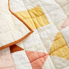 an orange and yellow quilt on top of a white bed cover with pink, yellow, and peach accents