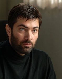 a close up of a person wearing a black shirt and looking at the camera with a serious look on his face