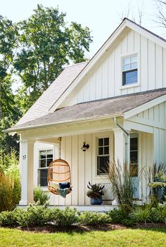 a white house with a hanging chair and plants in the front yard, on a sunny day