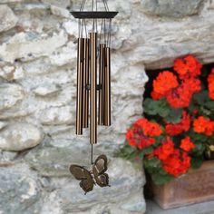 a wind chime hanging from the side of a stone building with flowers in front of it