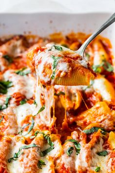 a spoon full of pasta and cheese being lifted from a casserole dish with spinach