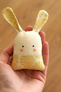 a hand holding a small stuffed animal in it's palm print fabric with an orange and white background