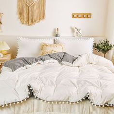 an unmade bed with white comforter and pom - poms on the headboard