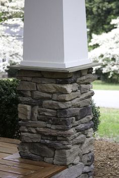 a wooden bench sitting next to a tall white pillar on top of a stone wall