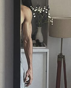 a man standing in front of a mirror next to a vase with flowers on it