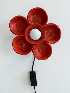 a red flower shaped object is plugged in to a wall charger with a white light on it