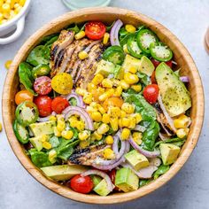 a wooden bowl filled with grilled chicken, avocado, corn and tomatoes