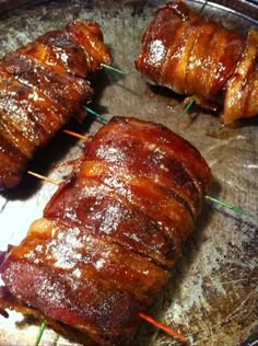 bacon wrapped meats on skewers sitting in a metal pan with toothpicks sticking out of them