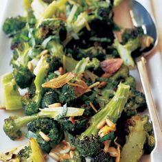 a white plate topped with broccoli and other vegetables next to a silver spoon