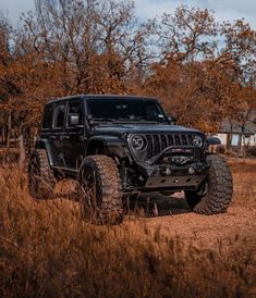 a black jeep is parked in the middle of a field with trees and grass behind it