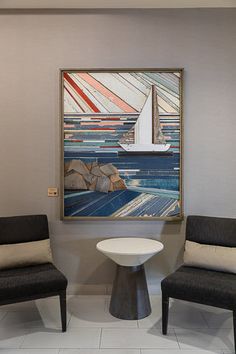 two chairs and a table in front of a wall with a painting hanging on it