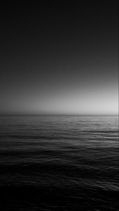 the sun is setting over the ocean on a dark, foggy day in black and white