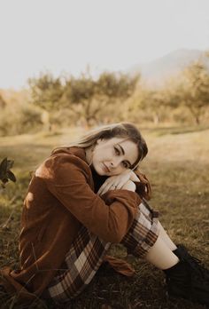 a woman is sitting on the grass with her hand under her chin