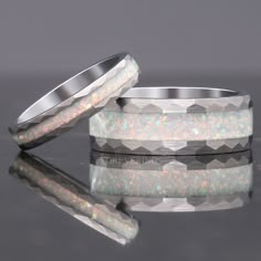 two wedding bands with white opal inlays are shown on a reflective surface