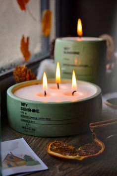 three lit candles sitting on top of a wooden table next to an orange and other items