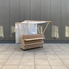 a wooden stand with a white sheet covering it on top of a tile floor in front of a gray wall