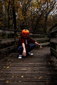 a person sitting on a wooden bridge with a pumpkin hat over their head and one hand in the air