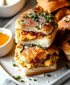 three sandwiches stacked on top of each other with sauce in the bowl next to them