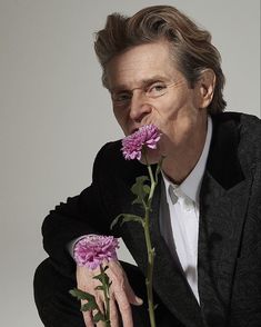 a man in a suit and tie holding a pink flower to his mouth with both hands