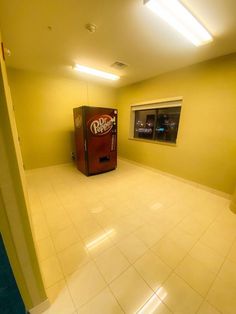 an empty room with a coke machine in the corner and no one around it on the floor