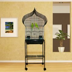 a bird cage with two green birds sitting on it's top shelf next to a potted plant