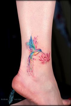 a small colorful bird tattoo on the side of a woman's foot with watercolors