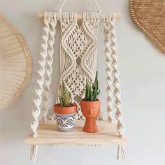 two potted plants sit on a shelf in front of a macrame wall hanging