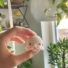 a hand holding a small crocheted object in front of a potted plant