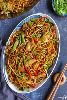 a plate full of noodles and chicken with chopsticks next to it on a table