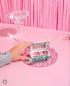 a woman's hand is holding onto a pink and green tray with makeup on it