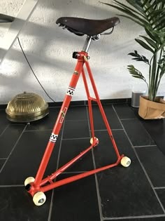 a red bicycle stand sitting on top of a black tile floor next to a potted plant