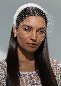 a woman wearing a birdcage veil on her head with long hair and earrings