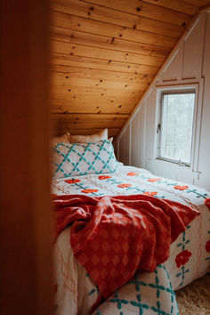 a bed in a room under a slanted ceiling with an orange and blue blanket on it