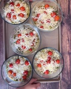 four glass bowls filled with food sitting on top of a pan covered in grated cheese