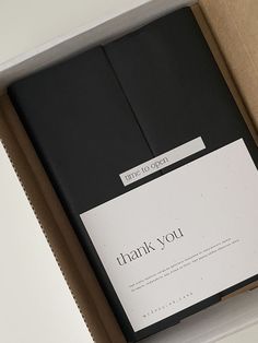 an open box containing two black notebooks with the words thank you written on them