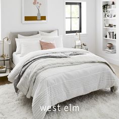 a bedroom with white bedding, pillows and pictures on the wall above it that says west elm