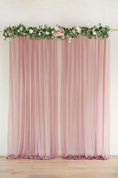 two pink drapes with flowers on them in front of a white wall and wooden floor